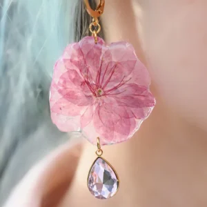 Każdy kolczyk kryje w sobie prawdziwy kwiat wiśni i różowy kryształ – unikatowa kompozycja zamknięta w żywicy.